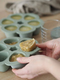 Main d'une personne qui demoule de la purée pour bébé conservée dans un moule en silicone multi portion  de la marque béaba