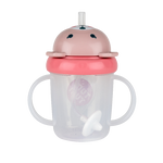 Tasse pour enfant de la marque Tum Tum sur fond blanc. La tasse est transparente avec des poignées de chaque coté et le logo de la marque au milieu. Elle a un couvercle bleu rabatable avec une tête d'ourson de couleur rose avec des oreilles en relief