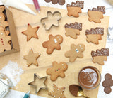 Table de cuisine avec des sablés de Noël posés dessus, il y a des sapins, des bonhommes  et des étoiles. Les biscuits sont décorés avec du chocolat