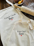 duo de tablier pour enfant et adulte. Des tabliers matchy matchy. Sur ke tablier adulte il est indiqué Grande Cheffe Mamie avec un coeur rouge et sur celui des enfants Petit Chef Ewenn
