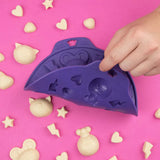 Gros plan sur une main qui démoule des petits chocolats blanc d'un moule en silicone violet. Le tout est posé sur une table de couleur rose