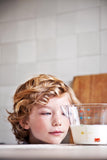 Photo d'un petit garçon ou l'on voit juste sa tête posée sur une table qui regarde un bol mesureur avec du lait à l'intérieur
