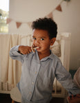 Phot d'un jeune garçons habillé d'une chemise de pyjama rayé bleu. Il tient dans sa bouche une brosse à dents avec une collerette de couleur beige. En arrière plan on aperçoit la chambre de l'enfant avec un lit bébé et un fanion accroché u mur