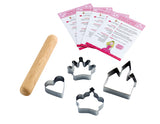 Contenu d'un coffret à patisserie pour enfant sur un fond blanc. Il y a 4 emportes-pièces en forme de coeur, chateau et couronnes. A coté un rouleau à patisserie en boie et sur le dessus 4 fiches de recette posées en éventail