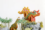3 biscuits sablés en forme de dinosaure en 3D, décorés avec glaçage de plusieurs couleurs. Les dinosaures en biscuits 3d décorés sont dans un décor de jungle artificielle: rocher, mousse et arbre.