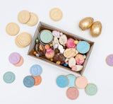 Photo d'une boîte à biscuit contenant des friandises et chocolats sur le thème de Pâque. A coté de la boite et éparpillé tout autour il y a des tampons a biscuits en silicone colorés ainsi que des sablés sur le même thème