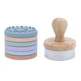 Kit de tampon pour biscuit posé sur un fond blanc, il y a les tampons en silicone colorés empilés les un aux autres et à coté son manche en bois avec son emporte pièce en acier