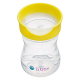 Tasse pour enfant transparent avec un couvercle transparent et un contour jaune. Elle est positionnée sur un fond blanc, la couvercle est plat et forme une coupelle