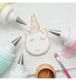 Photo d'un biscuit en forme de tête de licorne décoré a l'aide de glaçage coloré avec autour des douilles du glaçage