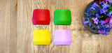 4 protèges doigts de la marque Opinel posé sur un plan de travail en bois, a coté d'un bouquet de fleurs. Les protèges doigt sont de couleurs rouge, vert, jaune et violet
