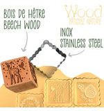 Tampon en bois en forme de dés en bois avec son découpoir en inox. Il est présenté dans son emballage. Le tampon represente des motifs de foret enchantée