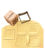 Pâte à sablé étalé avec des biscuits en forme de noel découpé dessus. Au dessus de la pâte il y a l'emporte pièce en inox qui a permeis de découper les biscuits ainsi que son tampon en bois en forme de dé