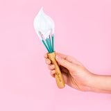 Photo d'une main tenant un fouet avec une crème fouettée sur la tête du fouet. La photo est prise devant un fond rose. Lefouet à un manche en bois gravé avec la marque chefclub et une tête bleu