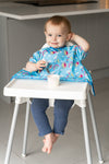 Jeune enfant assit sur une chaise haute et entrain de manger un yaourt. Il est habillé d'un bavoir de couleur bleu avec des illustrations d'arc en ciel et de soleil