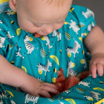 Gros plan sur le bavoir d'un bébé qui contient des morceaux de pastèques. Le tablier est de couleur bleu canard avec les couture jaunes et des illustration de zèbres dessus