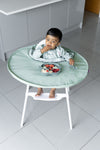 Jeune enfant entrain de manger dans une cuisine, il est assit sur une chaise haute équipé du plateau et de son bavoir intégrale de la marque Tidy Tot