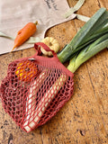 Filet de course de la marque Filt posé sur une table en bois, le sac de course contient des légues d'automne : poireaux, courge et carotte