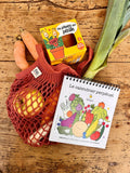Premiere page d'un calendrier perpétuel pour enfannt, il est illustré de fruist et légumes rigolos. Le calendrier est posé sur une table en bois ou il y a un filet de course avec des fruiits et légumes à l'intérieur ainsi qu'une boite contenant un kit de jardinage pour enfant