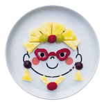 Assiette en porcelaine blanche avec une illustration de tête de bonhomme rigolos au centre. Elle est de la marque Cibolo , indiqué sur l’oval du visage. L’assiette permet de créer des repas rigolos en animant le personnage. Elle est composé de morceaux de fruits, representant une femme avec des lunettes et des bijoux