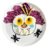 Assiette en porcelaine blanche avec une illustration de Monstre rigolos au centre. Elle est de la marque Cibolo , indiqué sur l’oval du visage. L’assiette permet de créer des repas rigolos en animant le personnage. Elle est composé d'une purée violette, de pointe d'asperge, d'oeuf et d'olive noire