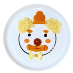 Assiette en porcelaine blanche avec une illustration de tête d’animal rigolos au centre. Elle est de la marque Cibolo , indiqué sur l’oval du visage. L’assiette permet de créer des repas rigolos en animant le personnage, elle est composée de semoule, carotte et tomate cerise. Elle represente un clown pas content