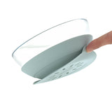 Photo d'un bol pour enfant en verre, avec une base en silicone qui contient une ventouse. La base est de couleur bleue, on voit un doigt qui retire et montre la base du bol pour enfant