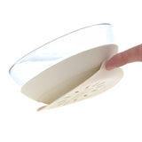 Photo d'un bol pour enfant en verre, avec une base en silicone qui contient une ventouse. La base est de couleur beige, on voit un doigt qui retire et montre la base du bol pour enfant