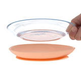 Photo d'une assiette pour enfant en verre, elle est tenue dans la main d'un adulte qui la retire de son socle en silicone de couleur rose