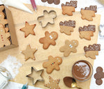 Table de cuisine avec des sablés de Noël posés dessus, il y a des sapins, des bonhommes  et des étoiles. Les biscuits sont décorés avec du chocolat