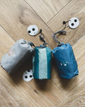 3 pochettes de 3 coussins nomades pour enfants sont posés sur un parquet en bois. ils sont de 3 motifs différents et disposent chacun de leur étiquettes de marque NouiNoui