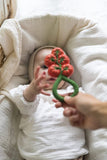 photo d'un bébé qui tend les mains pour attraper un jouet : hochet qui ressemble à une grappe de tomate