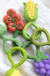 Ensemble de jouet de dentition de la marque Oli&Carol posés sur un lange blanc. il s'agit de hochet qui ont la forme de véritable fruits et légumes
