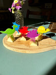 Ensemble de pics alimentaire pour enfant piqué sur des morceaux de pommes posés sur une planche en bois. Il y a 5 pics animaux