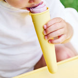 Gros plan sur une main d'enfant tenant une glace contenu dans un moule en silicone jaune