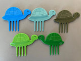 Ensemble de 5 pics alimentaires de différentes couleurs avec des formes de tortues. ils sont posés les uns devant les autres à plat sur une table de cuisine 