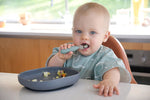 Bébé assis a table, entrain de manger à l'aide d'une fourchette