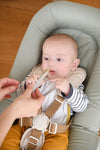 Bébé dans un transat qui attrape une cuillère en silicone grise tendu par la main d'un adulte