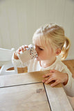 Photo d'une jeune enfant blonde qui boit dans un verre en plastique de couleur beige avec des illustrations de fleurs de jardin
