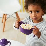Jeune enfant qui tient dans un bol à poignet de couleur violet, il contient des pop corn