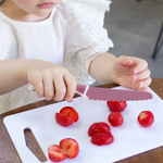 Gros plan sur les main d'une jeune fille qui coupe des fraises en morceaux a l'iade d'un couteau pour enfant de la marque kiddikutter de couleur rose