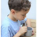 Jeune garçon entrain de boire à la paille dans un gobelet de la même couleur que la paille. Le garçon est habillé avec un tee shirt bleu, il a les cheveux brun et court