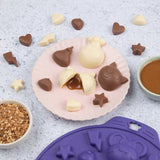 Photo d'une assiette contenant des chocolats en forme d'animaux. Le chocolat du milieux est un chocolat blanc ouvert en 2 avec du caramel qui dégouline