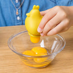 Gros plan sur la main d'un enfant qui depose un jaune d'oeuf dans un bol à l'aide d'une séparateur à oeuf de couleur jaune qui à la forme d'une poule