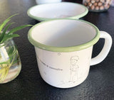 Photo d'un mug de couleur blanc avec les rebords arrondis et everre d'eau. Sur le mug il y a une illustration du Petot Prince avec un phrase d'inscrite. Le mug est posé sur une table de couleur grise avec a coté une petite plante posée dans un pot de yaourt