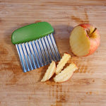 Coupe légumes avec lame ondulée posé sur une planche à découper en bois, avec sur sa lame des lamelles de pomme. Sur le côté une pomme a moitié decoupé
