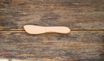 Couteau en bois brut, posé sur une table en bois foncé. Le couteau a une lame arrondie et il est entierement en bois