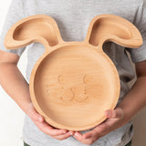 Assiette en bois pour enfant en forme de tête de lapin, elle possède 3 compartiments. L'assiette est tenu dans les main d'un enfant