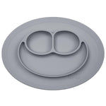 Photo d'un assiette avec plateau compartimenté de couleur grise sur fond bland. Elle comporte 3 compartiment, 2 petits et un grand. Sa forme est ovale, elle ressemble à un visage