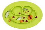 Photo d'un set de table avec assiette intégrée. Le set est de couleur vert. Son assiette est compartimentée en 3, il y a des reste d'aliments mangés dans chaque compartiment. Le set de table est de forme ovale, il ressemble a unvisage