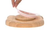 Dos d'une assiette en bambou en forme de souris. L'assiette a une ventouse en silicone de couleur rose. Sur le centre il y a des indication d'utilisation de gravé ainsi que le logo de la marque : Lässig. Il y a une main d'adulte qui soulève le joint en silicone.